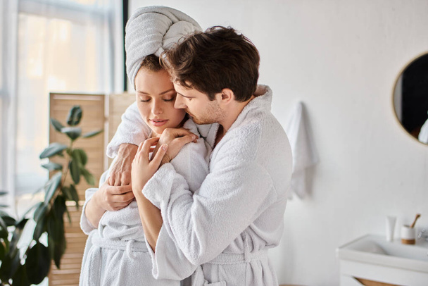 Portrait of happy man and woman in love in bathrobes in the bathroom, hugging each other - Foto, Imagem