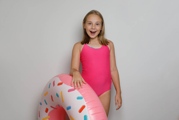 Joyful child girl with pink rubber inflatable ring swimming pool float standing on white studio wall background - Photo, Image
