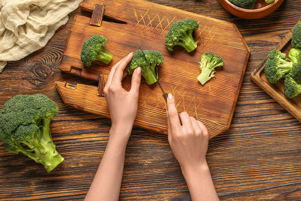 Woman cutting fresh broccoli cabbages on wooden background - Photo, Image