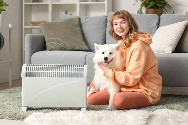 Fiatal nő Samoyed kutya felmelegedés mellett radiátor a padlón otthon - Fotó, kép