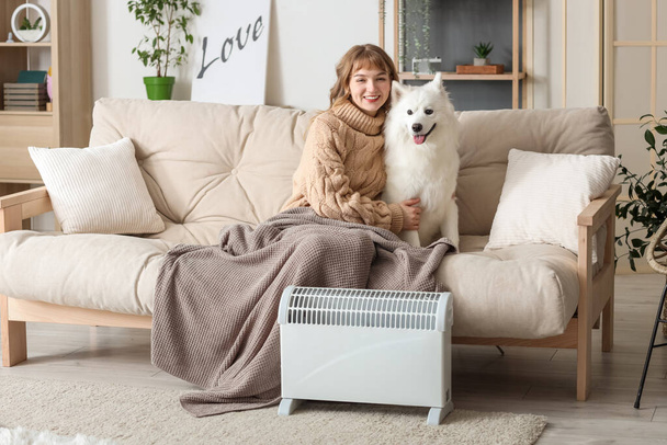 Молодая женщина в клетке и ее самоед собака на диване согревается возле радиатора дома - Фото, изображение