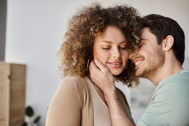 Ζευγάρι ερωτευμένο με όμορφο άντρα και σγουρή γυναίκα στο σπίτι το πρωί, χαμογελώντας και αγκαλιάζοντας - Φωτογραφία, εικόνα