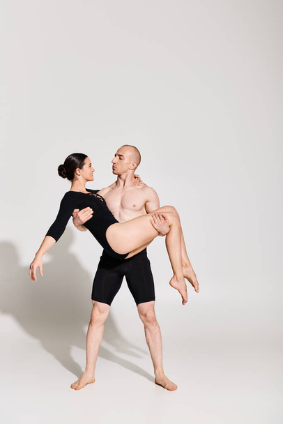 A shirtless young man holds a woman in an acrobatic dance pose, showing strength and grace in a studio setting on a white background. - Photo, Image