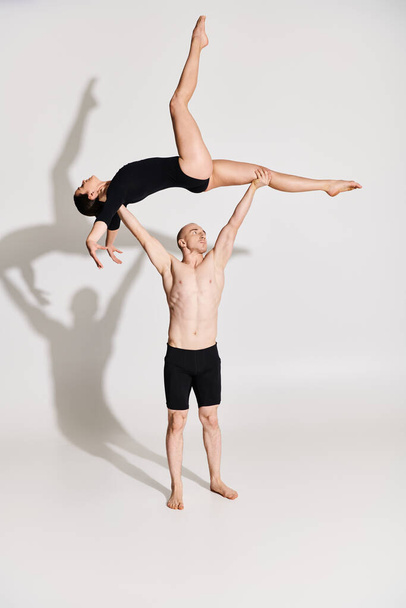 Young shirtless man holding a young woman, showcasing agility and balance in a studio setting against a white background. - Photo, Image