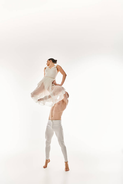 Młody mężczyzna bez koszuli i kobieta w białej sukience tańczą razem, wykonując akrobatyczne elementy w studio na białym tle. - Zdjęcie, obraz