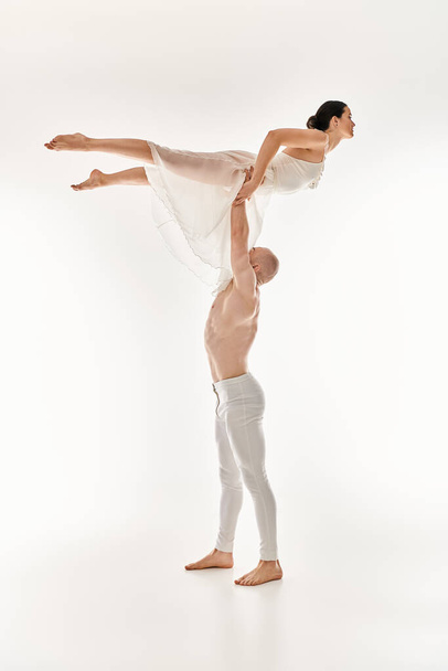 Egy félmeztelen fiatal férfi és egy fehér ruhás nő dinamikus és akrobatikus táncgyakorlatot folytat stúdióban.. - Fotó, kép