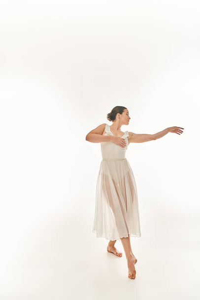 Jonge vrouw in elegante witte jurk wervelt terwijl het houden van een witte frisbee, tegen een witte achtergrond. - Foto, afbeelding