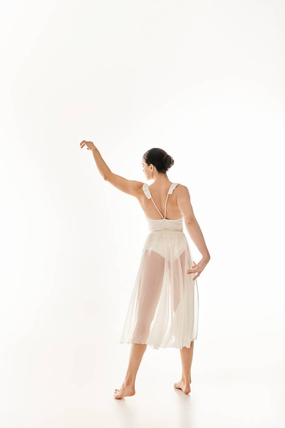 Una joven mujer bailando cautivadoramente en su largo vestido blanco sobre un fondo blanco. - Foto, imagen