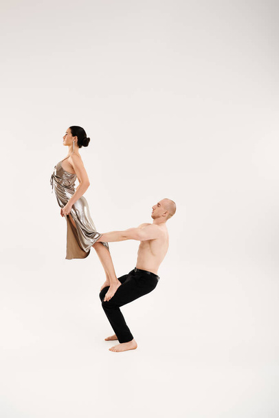 Un homme torse nu et une femme dans une robe brillante faisant élément acrobatique dans un cadre de studio. - Photo, image