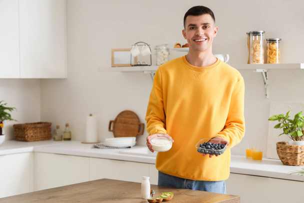 Fiatal férfi ízletes joghurttal és áfonyával a konyhában - Fotó, kép