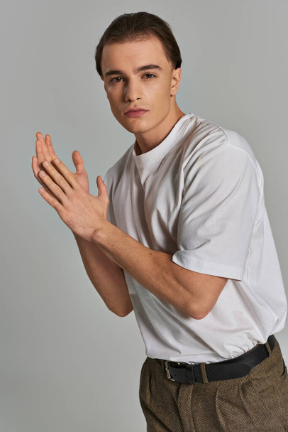fashionable young male model in sophisticated pants looking at camera while on gray background - Photo, Image