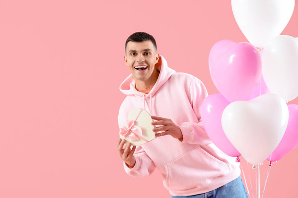 Красивий чоловік з подарунковою коробкою і повітряними кулями на рожевому тлі. Святкування Дня святого Валентина - Фото, зображення