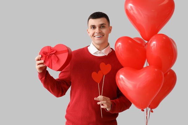 Jóképű férfi ajándékkal, szívekkel és lufikkal, könnyű háttérrel. Valentin-napi ünneplés - Fotó, kép