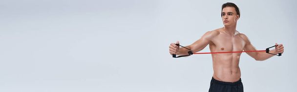 kuszący sportowiec bez koszulki w czarnych spodniach trening z ekspanderem fitness i odwracanie wzroku, baner - Zdjęcie, obraz