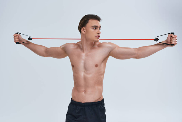 csábító félmeztelen sportos fiatalember fekete nadrágban edzés fitness expander és félrenéz - Fotó, kép