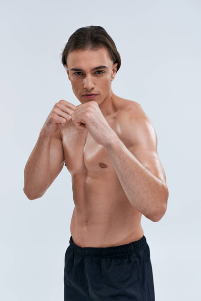 handsome sexy sporty man in black pants posing topless with fists in front of him looking at camera - Photo, Image