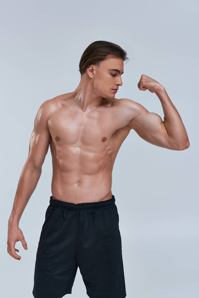 sexy bez koszulki sportowiec człowiek w czarny spodnie gra jego mięśnie podczas pozowanie na szary tło - Zdjęcie, obraz