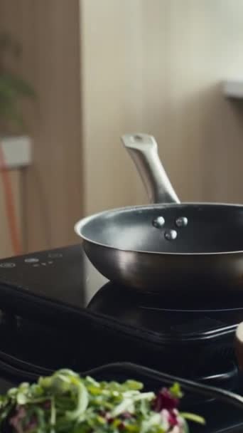Vertikální zblízka záběr rukou člověka nalévání vajíček z mísy na pánvi horké vaření při přípravě jídla v kuchyni - Záběry, video