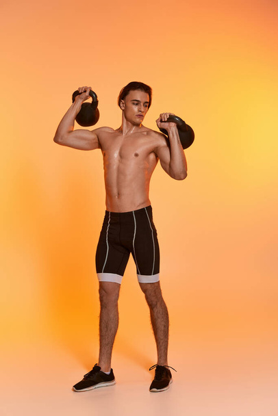 hombre sin camisa deportivo guapo haciendo ejercicio con pesas y mirando hacia otro lado en el fondo naranja - Foto, imagen