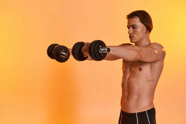 attractive muscular shirtless man in black sport shorts training with dumbbells on vivid backdrop - Photo, Image