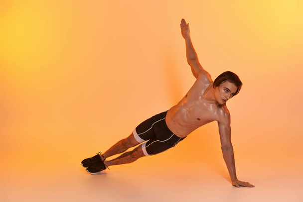 homem sem camisa de boa aparência em shorts pretos exercitando ativamente e olhando para o fundo laranja - Foto, Imagem