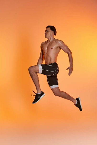 appealing shirtless man in black shorts exercising actively and looking away on orange backdrop - Photo, Image