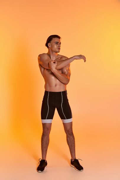 komea paidaton mies mustissa shortseissa harjoitellen aktiivisesti ja katsellen oranssia taustaa - Valokuva, kuva
