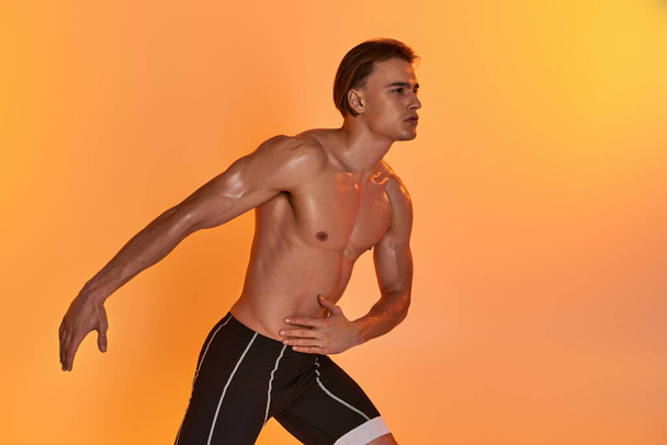 hyvännäköinen nuori urheilullinen mies poseeraa yläosattomissa aktiivisissa liikkeissä oranssilla eloisalla taustalla - Valokuva, kuva