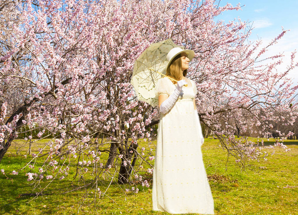 Nainen valkoinen historiallinen mekko valkoinen sateenvarjo vaaleanpunainen kevät puita kukka. - Valokuva, kuva