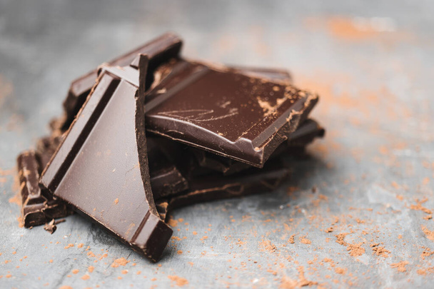 Haufen köstlicher dunkler Schokoladenstücke oder Würfel, gehackt, gebrochener Schokoladenriegel auf dunklem Hintergrund. - Foto, Bild