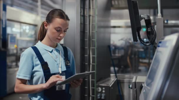 Közepes oldalsó szúrás felvétel egy fehér nő gyártómérnökről, aki táblagépen dolgozik, és a gyártási folyamatot a gyár monitorján állítja be. - Felvétel, videó