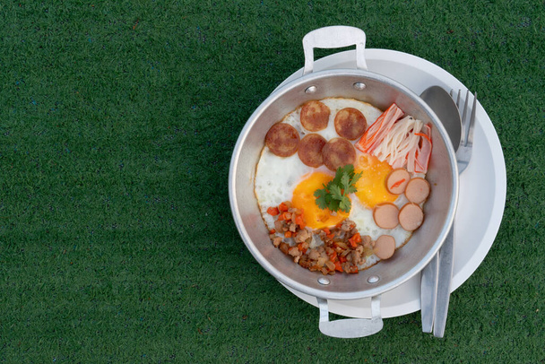 Жареные яйца сверху со свининой, горячими цветами, китайской колбасой и крабовыми палочками. Подается в оцинкованной пластине и помещается на тарелку. Размещен на искусственной траве - Фото, изображение