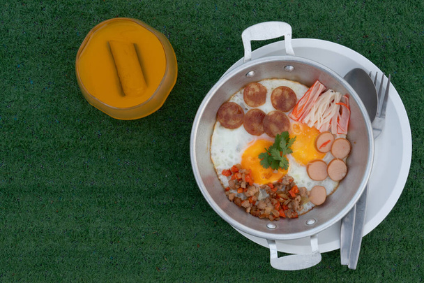Жареные яйца сверху со свининой, горячими цветами, китайской колбасой и крабовыми палочками. Подается в оцинкованной пластине и помещается на тарелку. Подается с апельсиновым соком. Размещен на искусственной траве - Фото, изображение