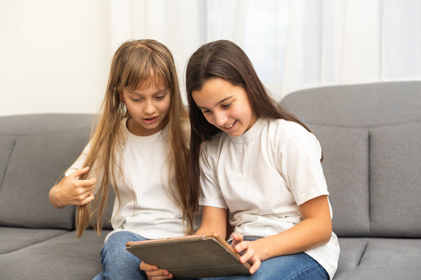 Young twins using a laptop and a tablet sitting on a couch in the living room. High quality photo - Photo, Image