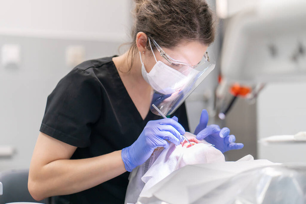O dentista examina a boca e os dentes do paciente usando um explorador dentário. Exame dentário preventivo periódico de dentes e gengivas para prevenção de cárie e doenças periodontais. - Foto, Imagem