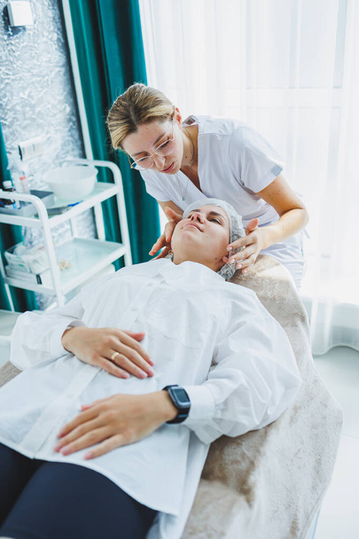 Uma jovem mulher numa consulta com um esteticista. Um cosmetologista faz uma massagem facial ao cliente. Facial. Uma viagem ao esteticista. - Foto, Imagem