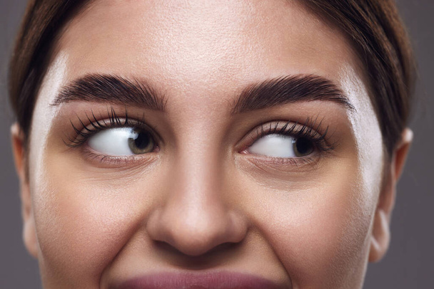 Foto cortada. Close-up de olhos de mulheres com sobrancelhas bem tratadas, olhos claros e pele lisa contra um fundo cinza. Conceito de médico, exercícios de técnicas de visão, e focagem para os olhos. - Foto, Imagem