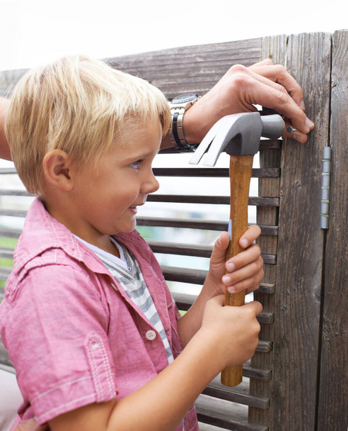 Niño feliz, martillo y niño haciendo mantenimiento en la puerta de madera para la diversión o el aprendizaje. Sonrisa, equipo y niño pequeño mirando y trabajando en reparaciones con la herramienta para la mejora del hogar al aire libre en la casa moderna - Foto, imagen