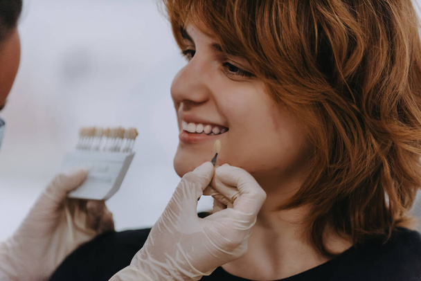 Стоматолог экспериментирует с новыми оттенками зубов для протезирования в стоматологическом кабинете, демонстрируя точность и инновации в лечении зубов. - Фото, изображение