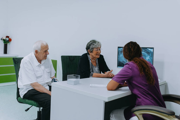 An elderly couple engages in a thoughtful discussion with their dentist about modern denture options in a contemporary dental office setting. - Photo, Image
