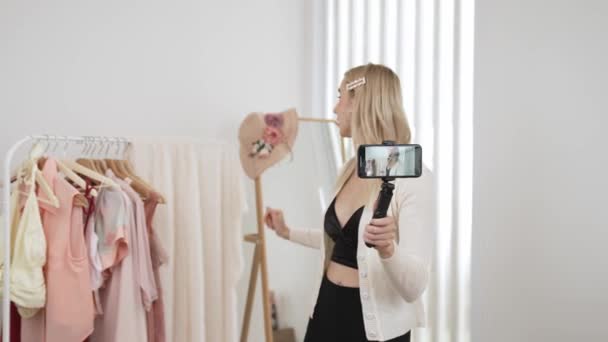 Νεαρή γυναίκα δημιουργός περιεχομένου κοινωνικών μέσων κάνει βίντεο μόδας χρησιμοποιώντας selfie ραβδί. Blogger χαμόγελο στην κάμερα, ενώ κάνοντας πειστική σε απευθείας σύνδεση ρούχα πωλούν vlog στο κοινό ή οπαδός. Κυψέλη - Πλάνα, βίντεο