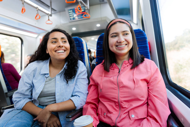 Twee jonge Latijnse vrouwelijke studenten of pendelaars die met het openbaar vervoer in de stad reizen en een mobiele telefoon gebruiken. Hoge kwaliteit foto - Foto, afbeelding