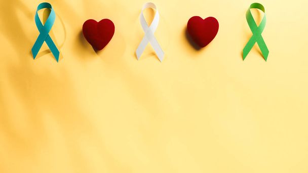 Κορδέλα και καρδιά σε κίτρινο φόντο για την ημέρα ευαισθητοποίησης του καρκίνου. - Φωτογραφία, εικόνα