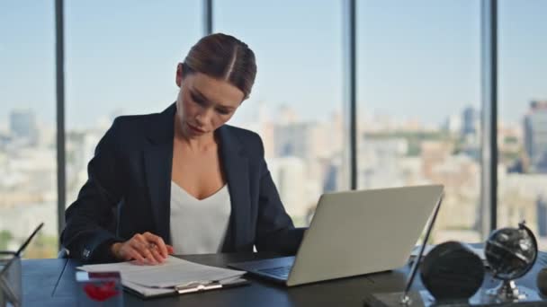 Pensive lady working laptop doing paperwork. Successful businesswoman checking online report working in panoramic office. Marketing professional analysing study documents at desk. Female ceo career - Footage, Video