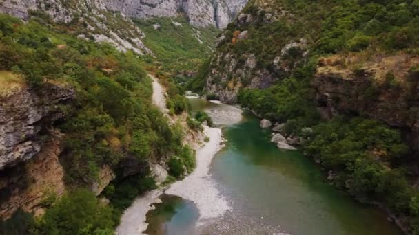 Luchtfoto drone uitzicht op schorsing oude metalen brug in het midden van prachtige rotsachtige canyon met turquoise rivier, Montenegro. Moraca rivier canyon met groene levendige vegetatie - Video