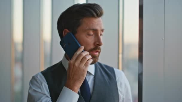 パノラマのオフィスの窓で携帯電話を話すポートレートの自信を持ったリーダー. ビジネス上の問題について話し合うハンサムな男性コンサルタント. 成功した中年銀行家ビジネスマン話しセル  - 映像、動画