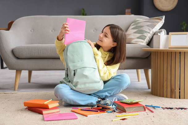 Petite écolière mettant copybook dans un sac à dos à la maison - Photo, image