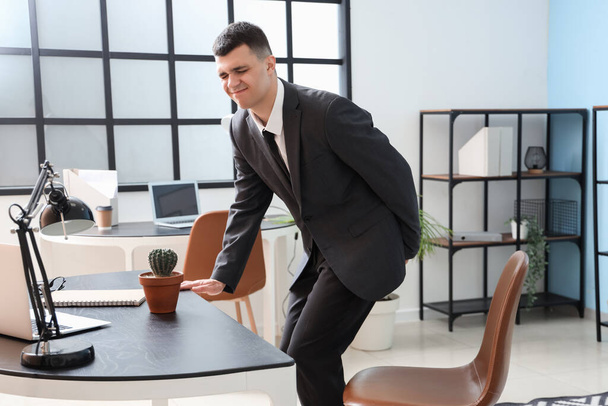 Young businessman with hemorrhoids sitting on chair in office - Foto, imagen