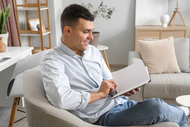 Mladý muž čte knihu v křesle doma - Fotografie, Obrázek