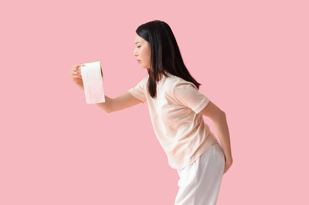 Young Asian woman with hemorrhoids and toilet paper on pink background - Photo, Image